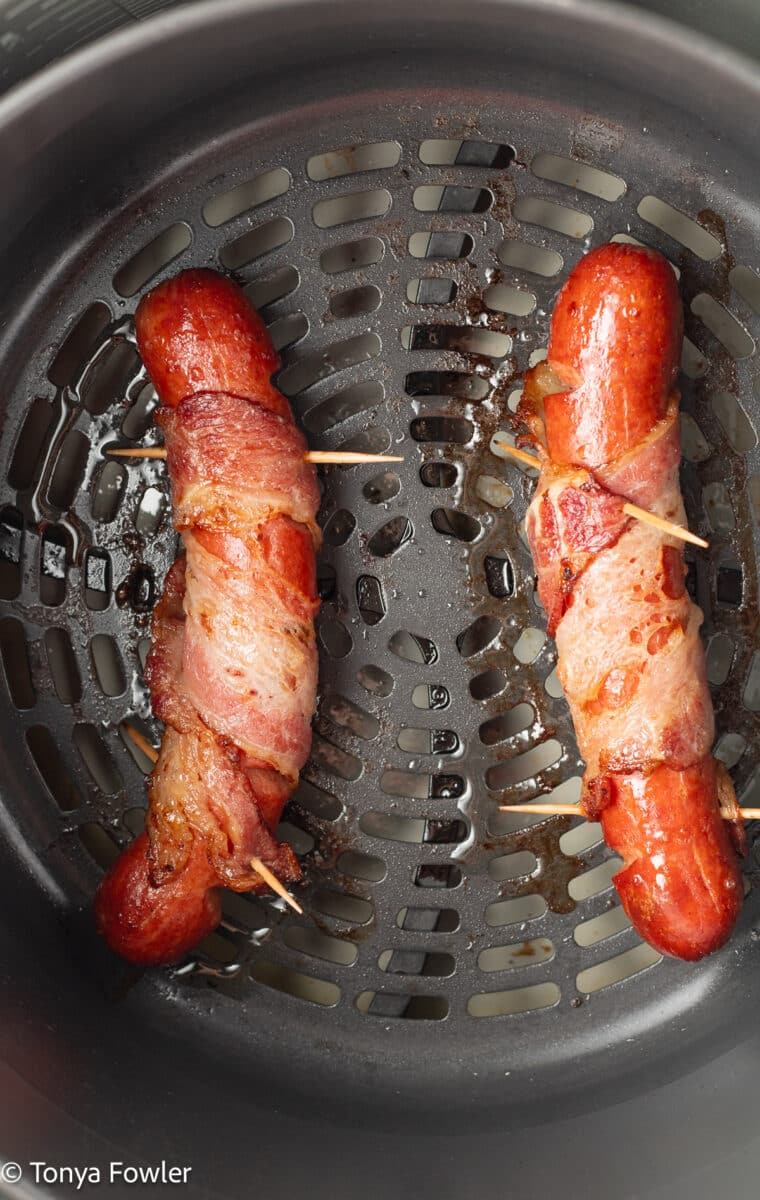 Cooked hot dogs in an air fryer basket.
