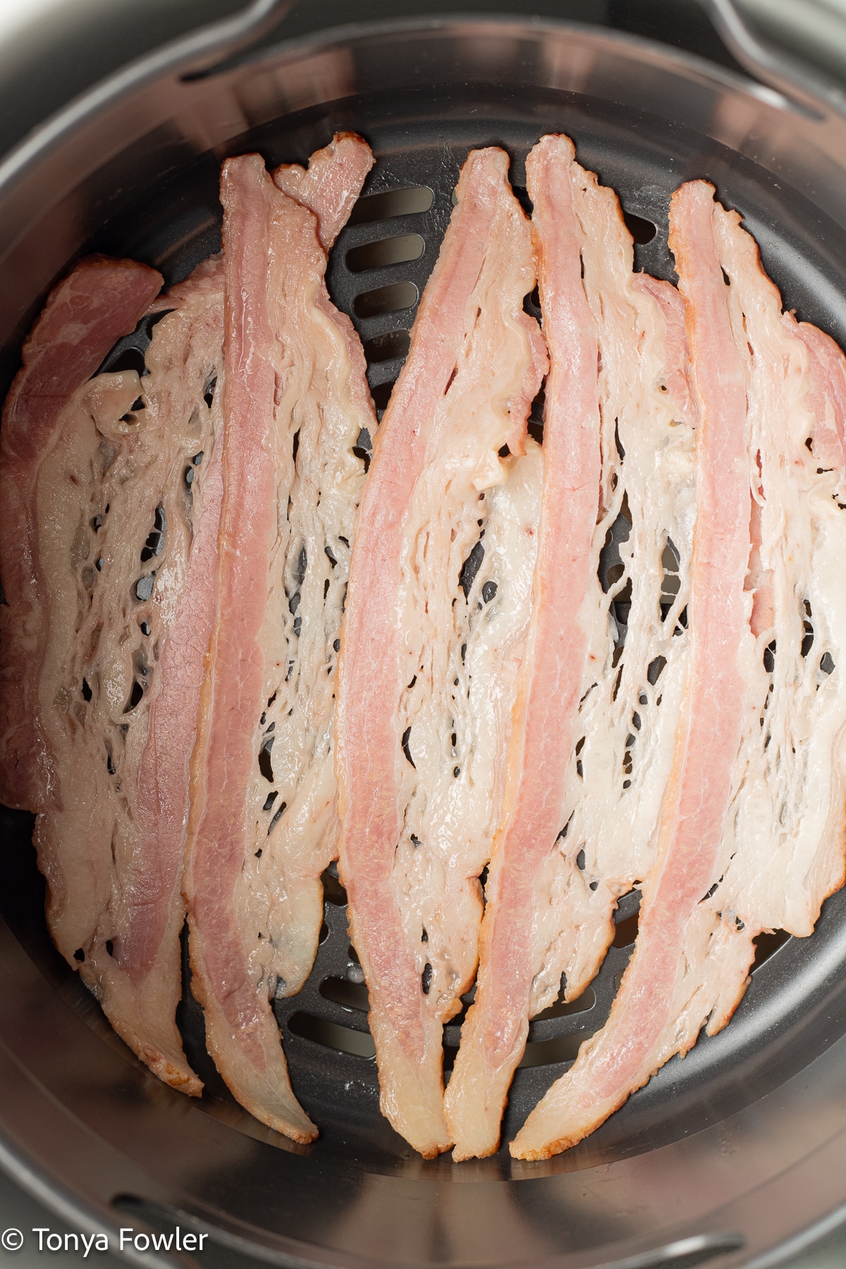Raw bacon in an air fryer basket.