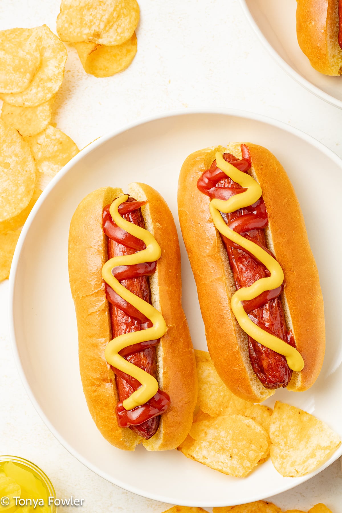Hot dogs on a plate with chips.