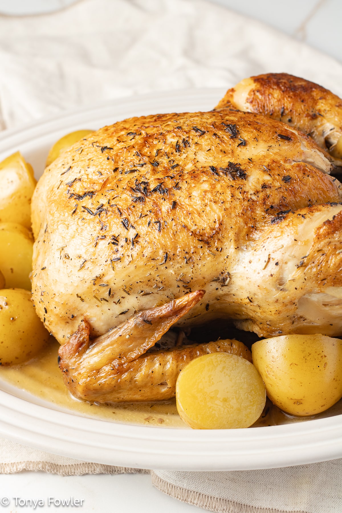Dutch oven whole roast chicken on a platter with potatoes.
