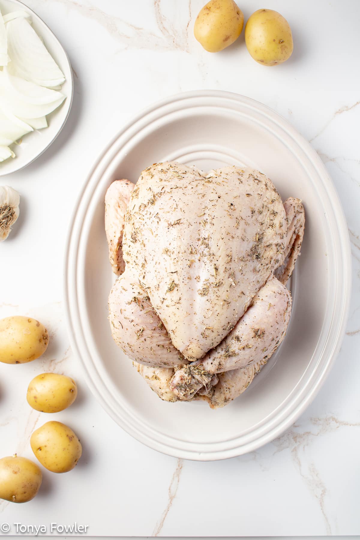 Uncooked chicken on a platter rubbed with herbs.