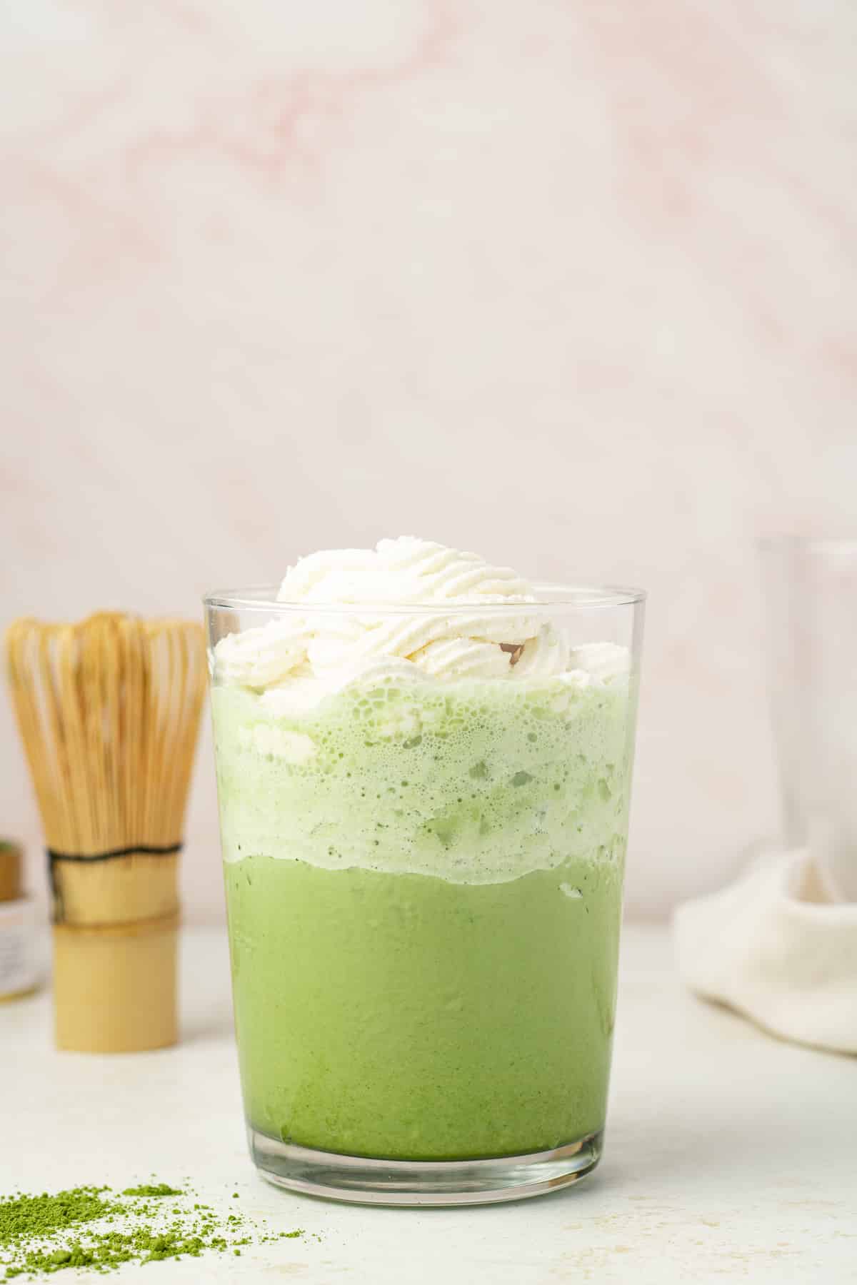 Side view of a matcha frappe in a glass topped with whipped cream.