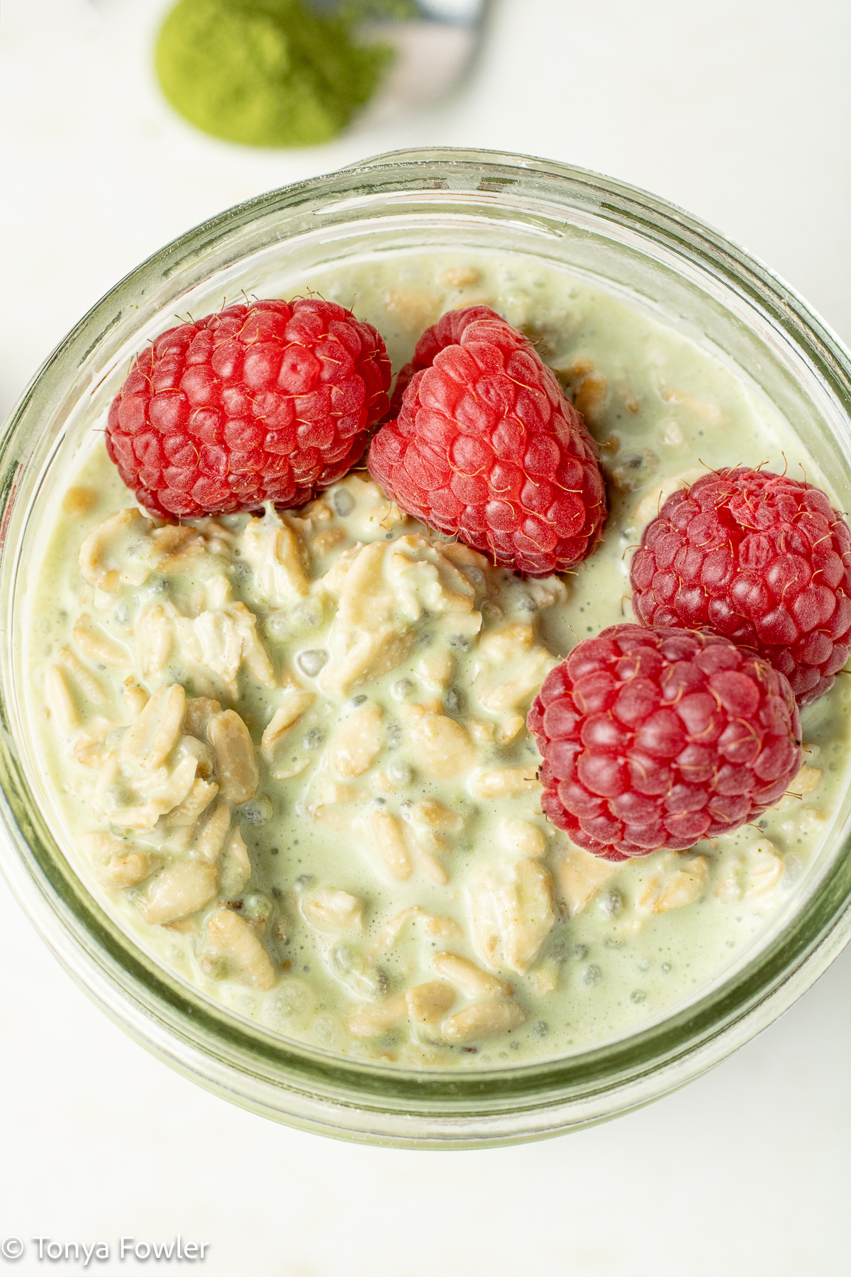 Close up image of oats in a jar topped with raspberries.