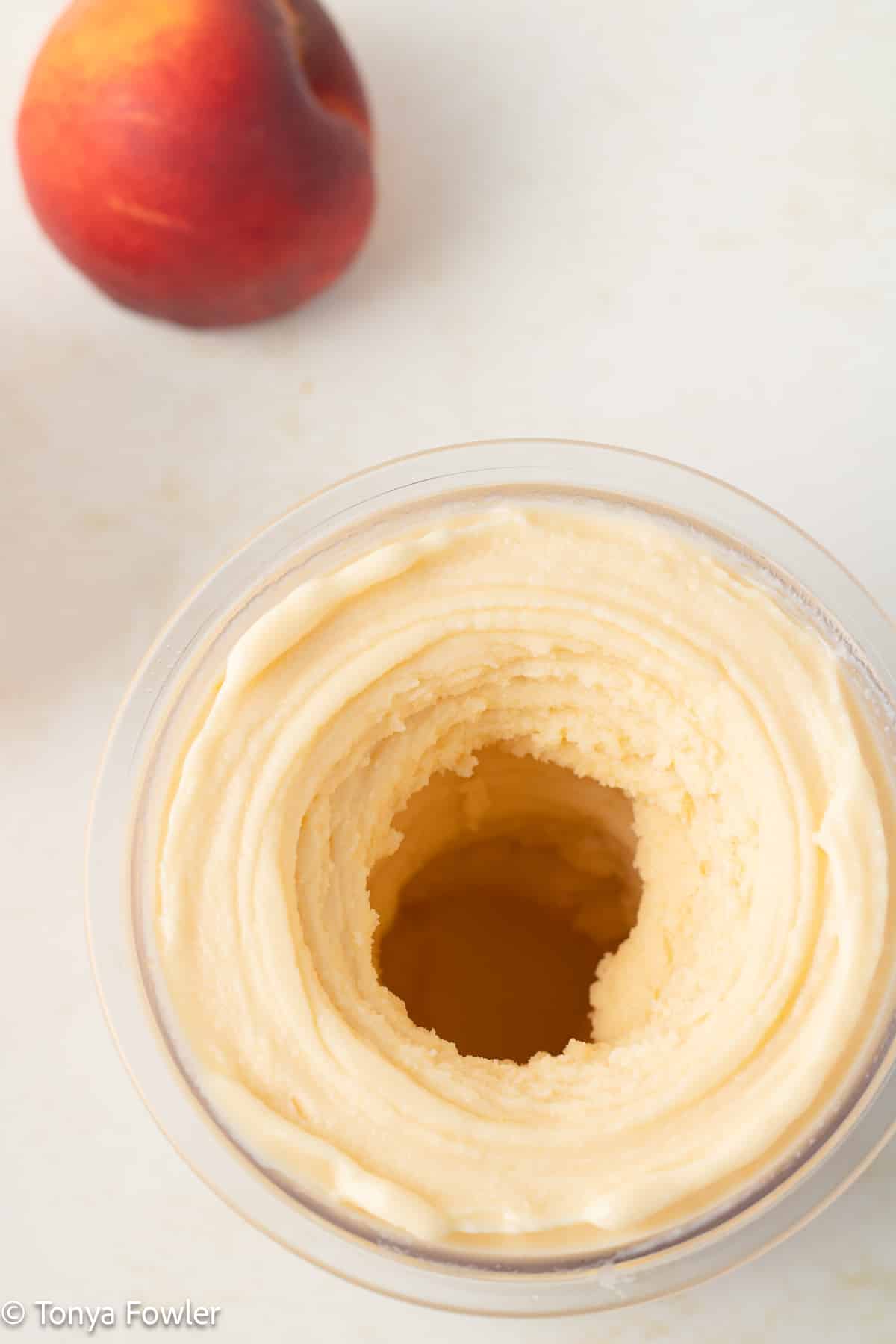 Blended frozen yogurt in a container with a fresh peach near by.