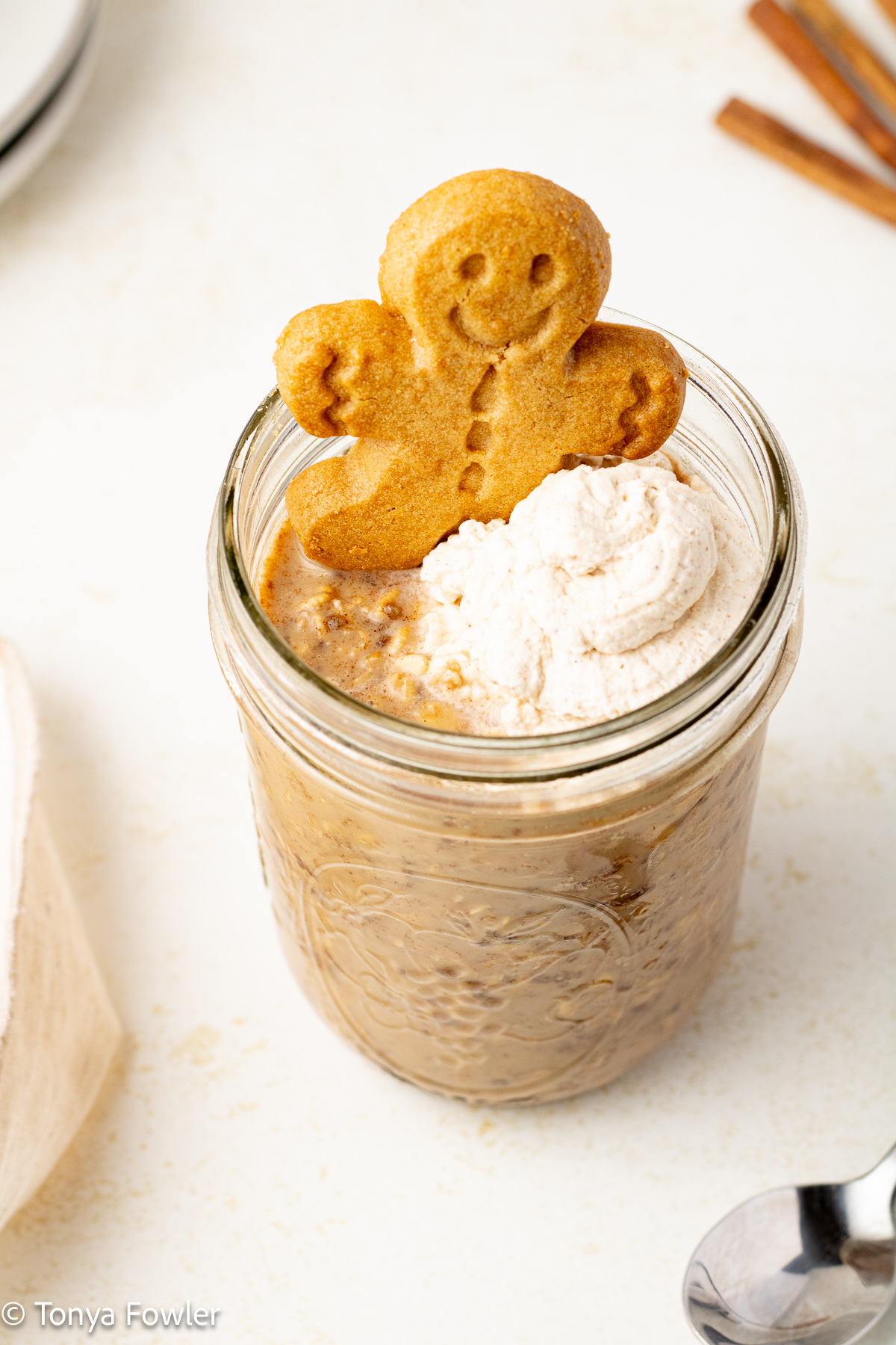 Overnight oats in a mason jar topped with whipped cream and a gingerbread man cookie.