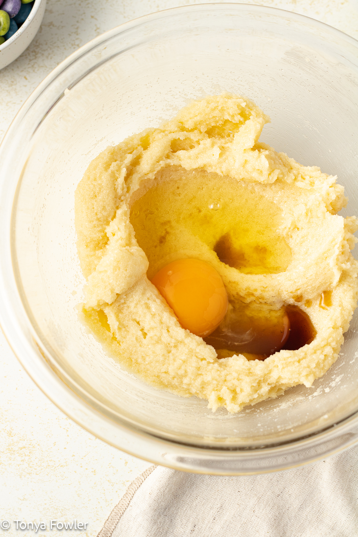 Creamed butter and cream in a bowl with an egg and vanilla extract on top.