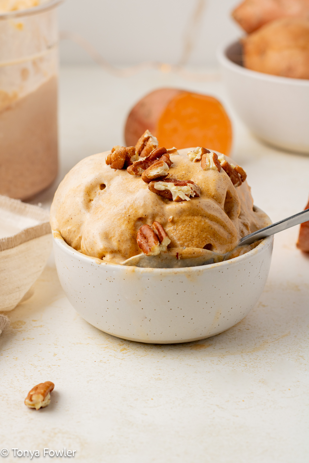Straight on view of scoops of ice cream in a bowl with a spoon topped with nuts.