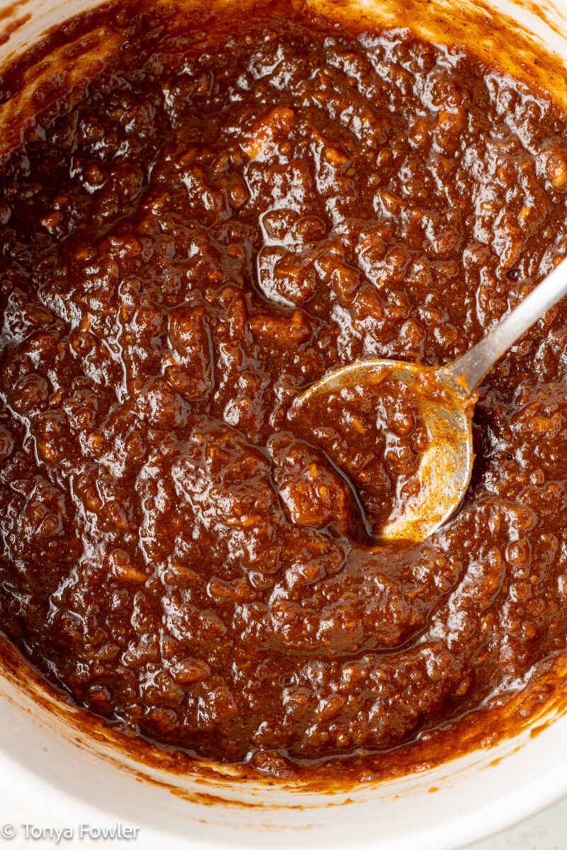 Sweet potato, sugar and spices mixed together in a bowl with a spoon.
