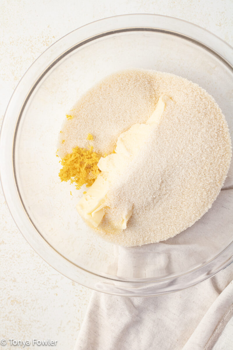 Granulated sugar, lemon and lemon zest in a bowl. 