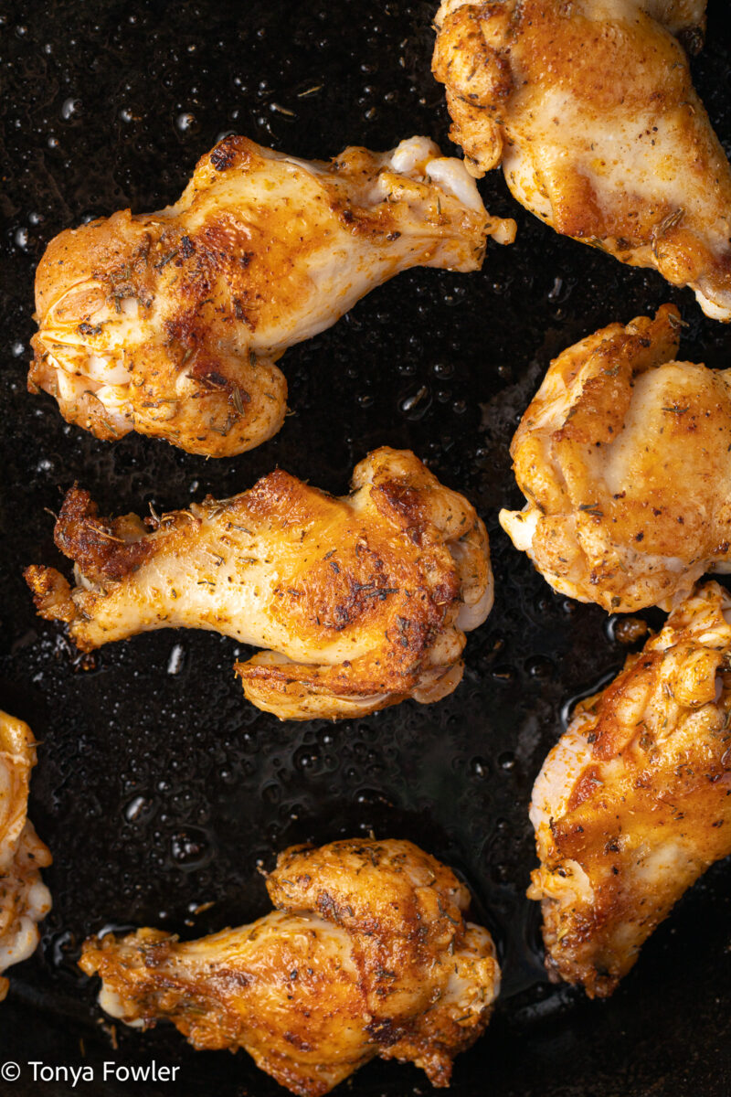Close up image of browned chicken wings in a skillet.