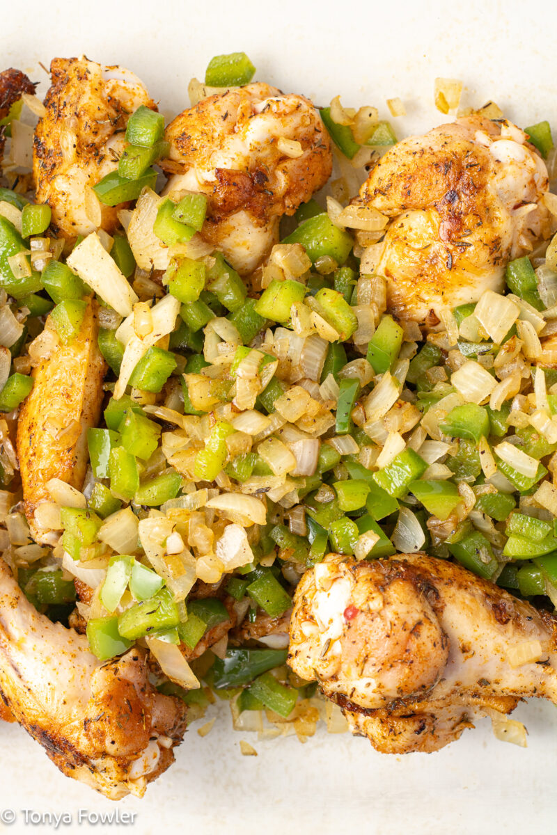 Chicken wings in a baking dish topped with onions and bell peppers.