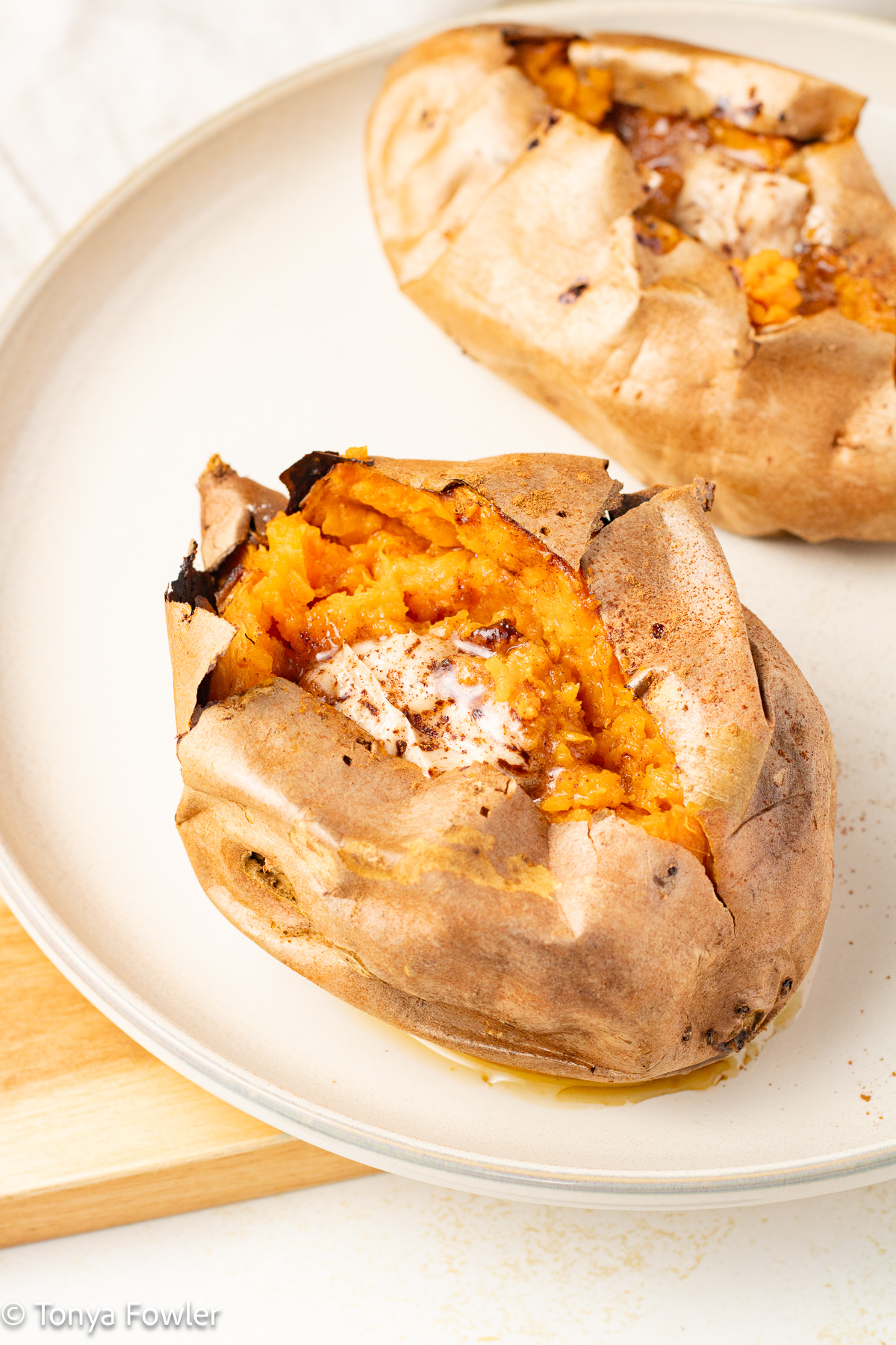 Baked sweet potatoes on a plate split open, topped with butter and sprinkle of ground cinnamon.