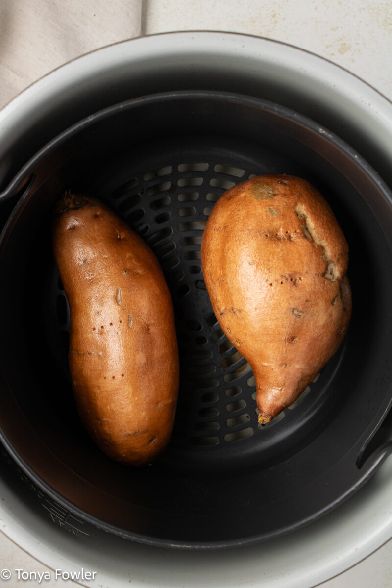 Whole sweet potatoes in an air fryer basket.