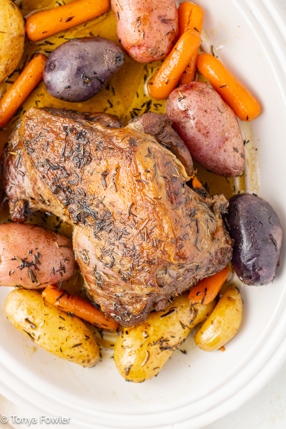 Overhead view of braised lamb on a platter with potatoes and carrots.