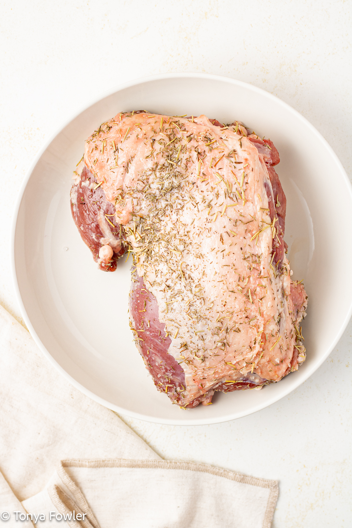 Uncooked raw piece of lamb rubbed with herbs sitting on a plate.