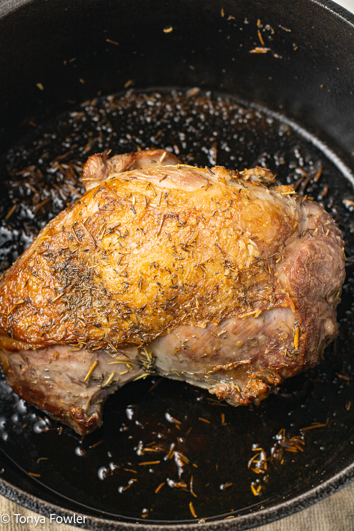 Close up image of a cooked piece of lamb in a cast iron dutch oven.