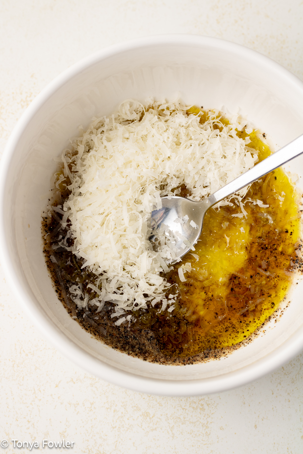 Grated parmesan cheese, avocado oil and mustard in a bowl with a spoon.