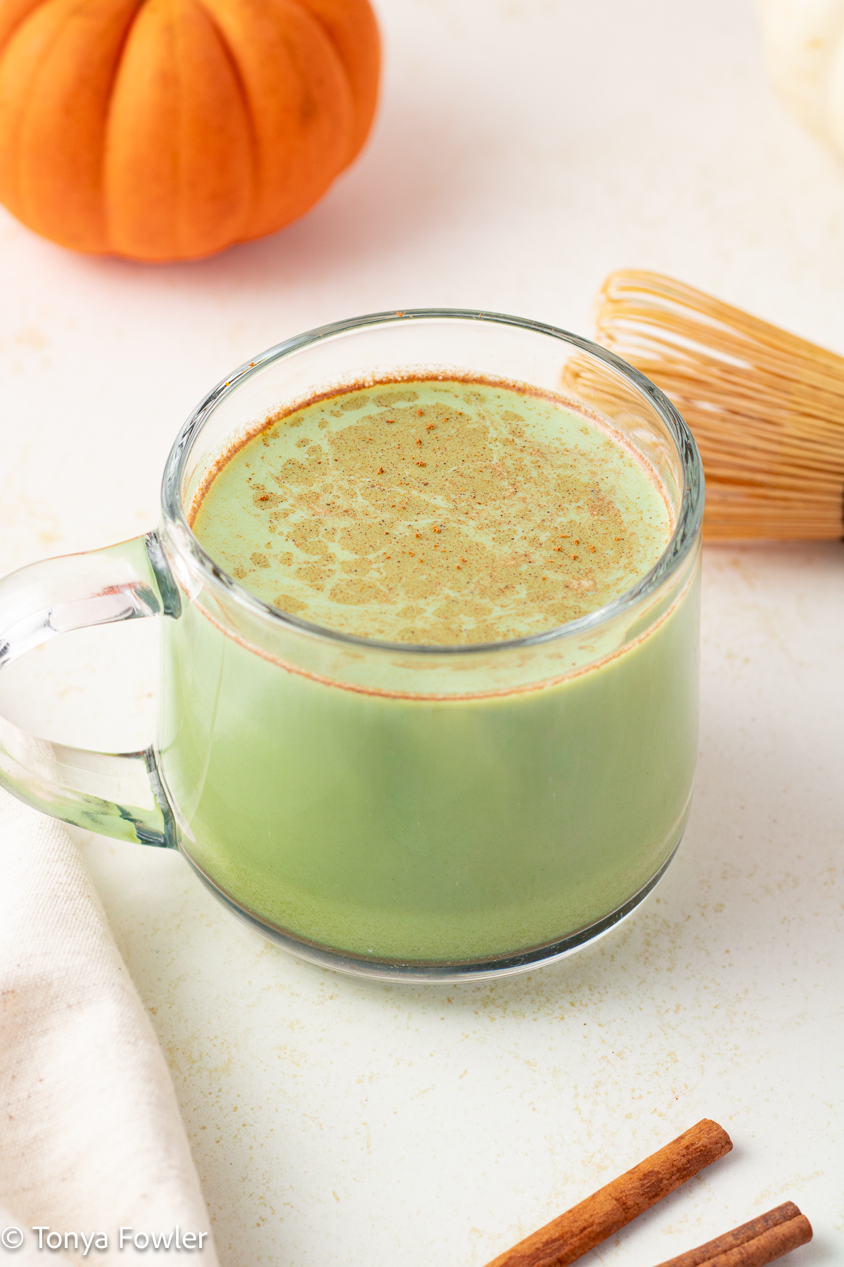 3/4 view of a matcha latte surrounded by a pumpkin and whisk.