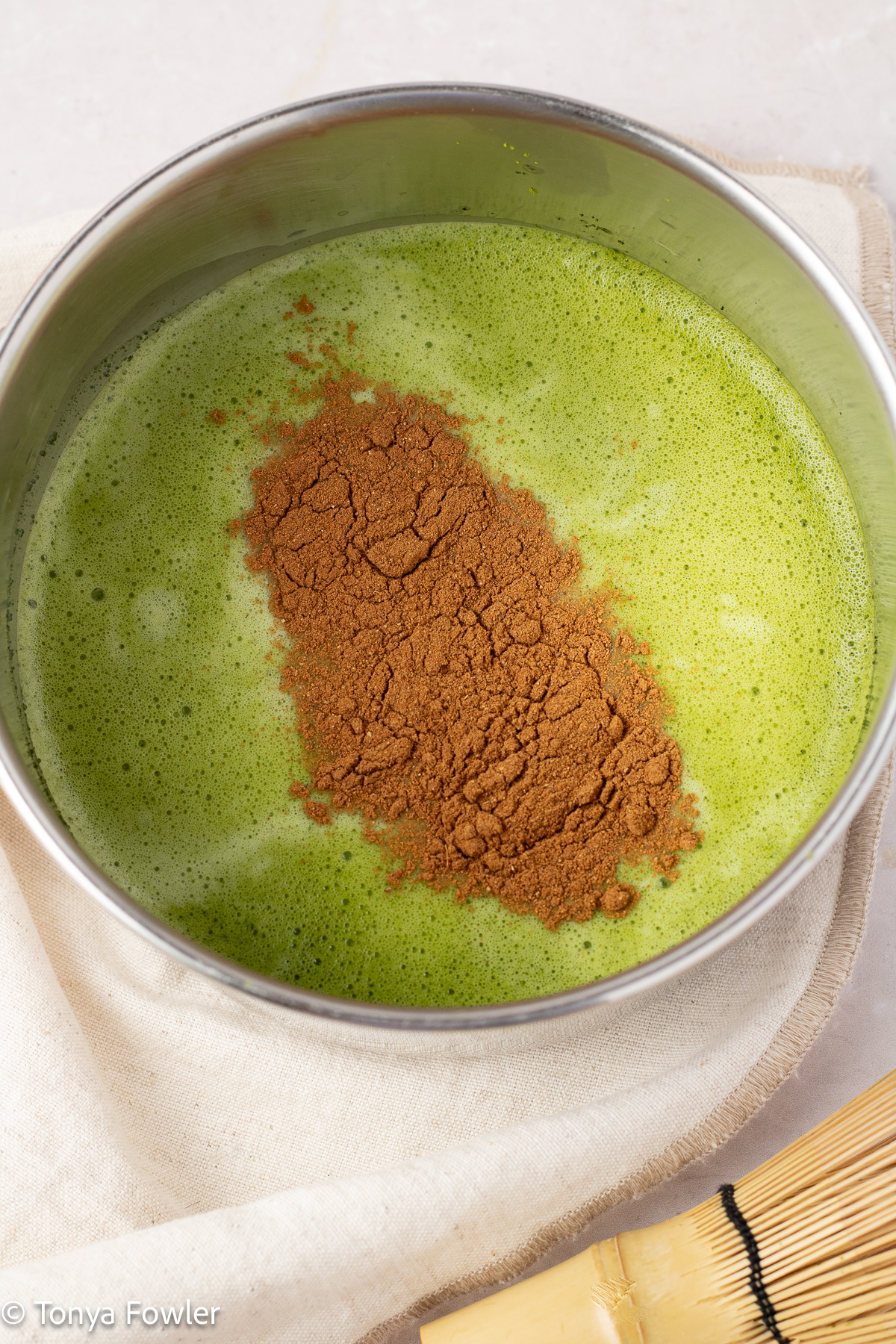 Matcha powder mixed with water topped with pumpkin spice mix in a pot.
