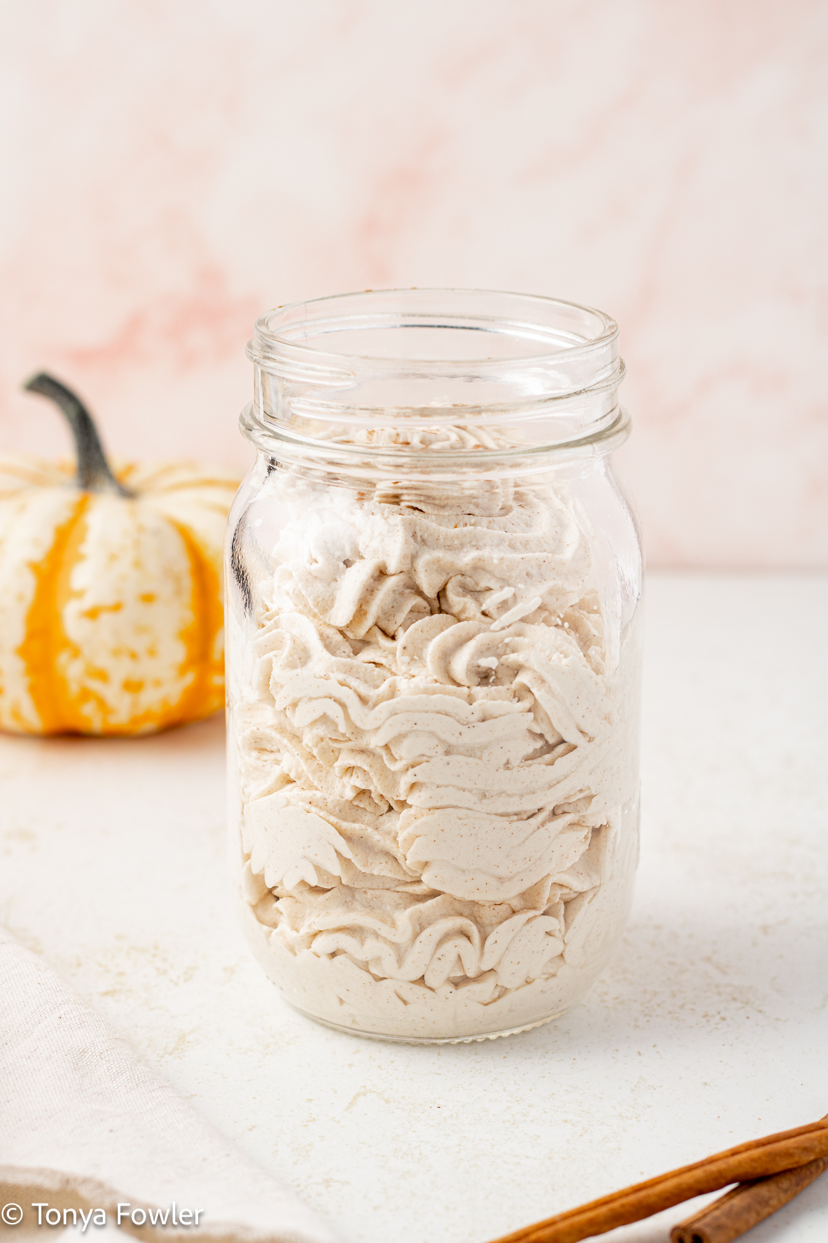 Straight on view of pumpkin spice whipped cream in a mason jar with a pumpkin in the background.