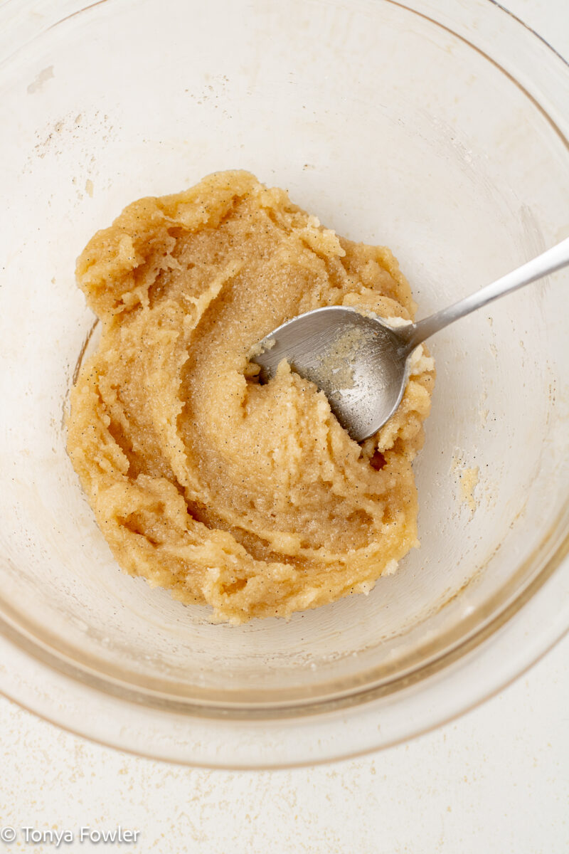 Sugar, cream cheese, and vanilla mixed together in a bowl with a spoon.