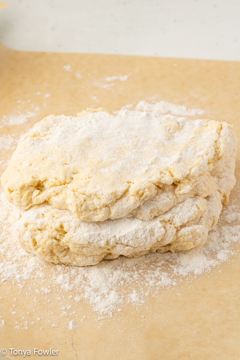 Biscuit dough folded on a piece of parchment paper dusted with flour.