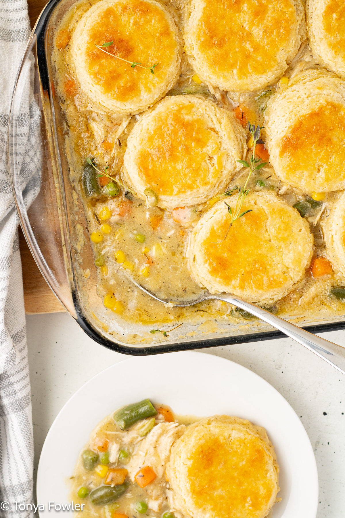 Pot pie in a baking dish with a spoon. Biscuit and filling on a plate near by.