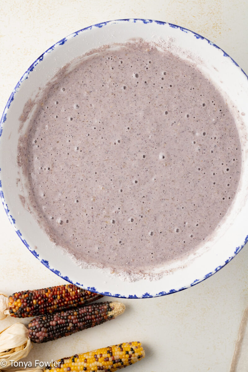 Cornmeal batter in a bowl with decorative corn cobs on the table near by.