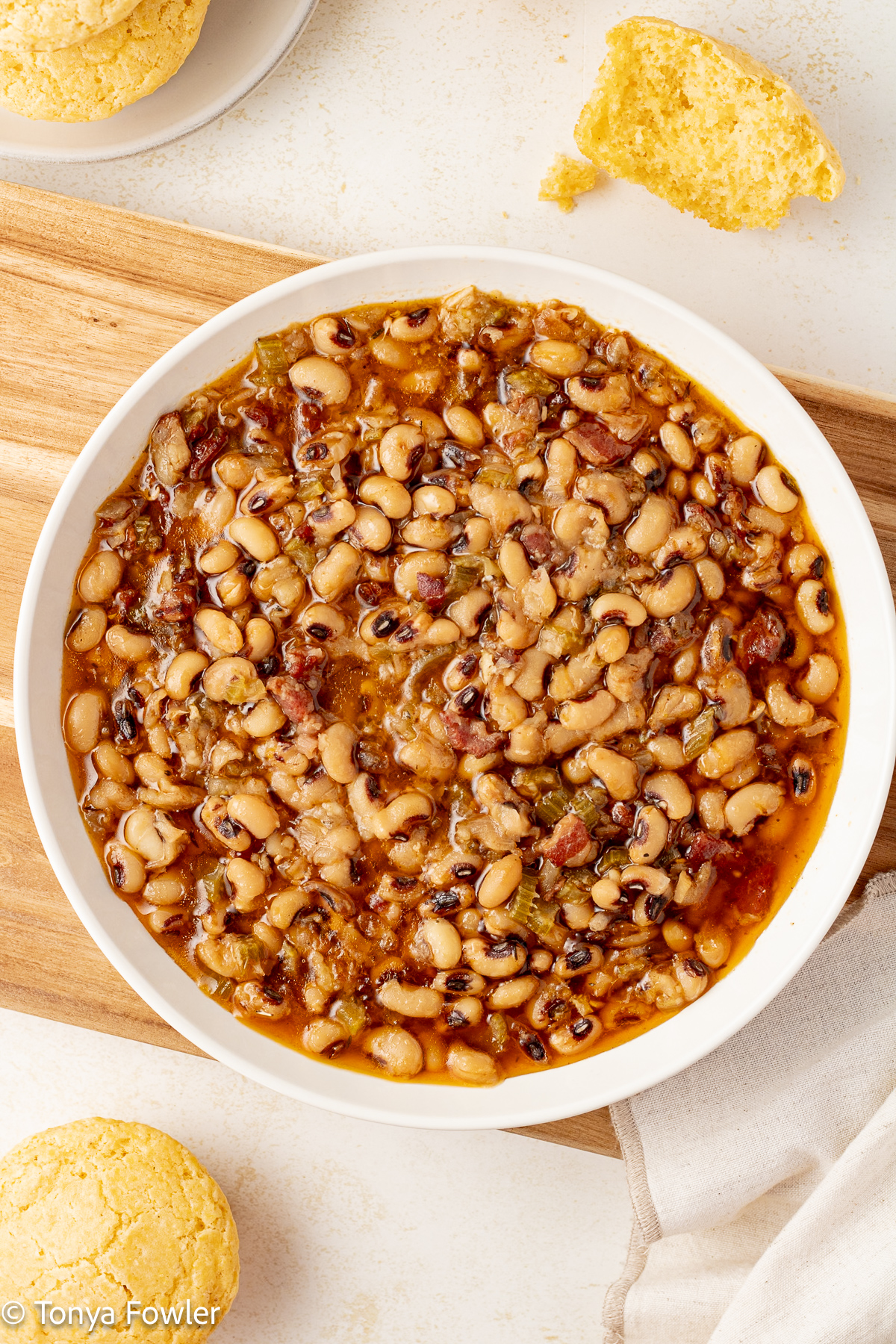 Black eyed peas in a bowl with cornbread muffins on the counter.