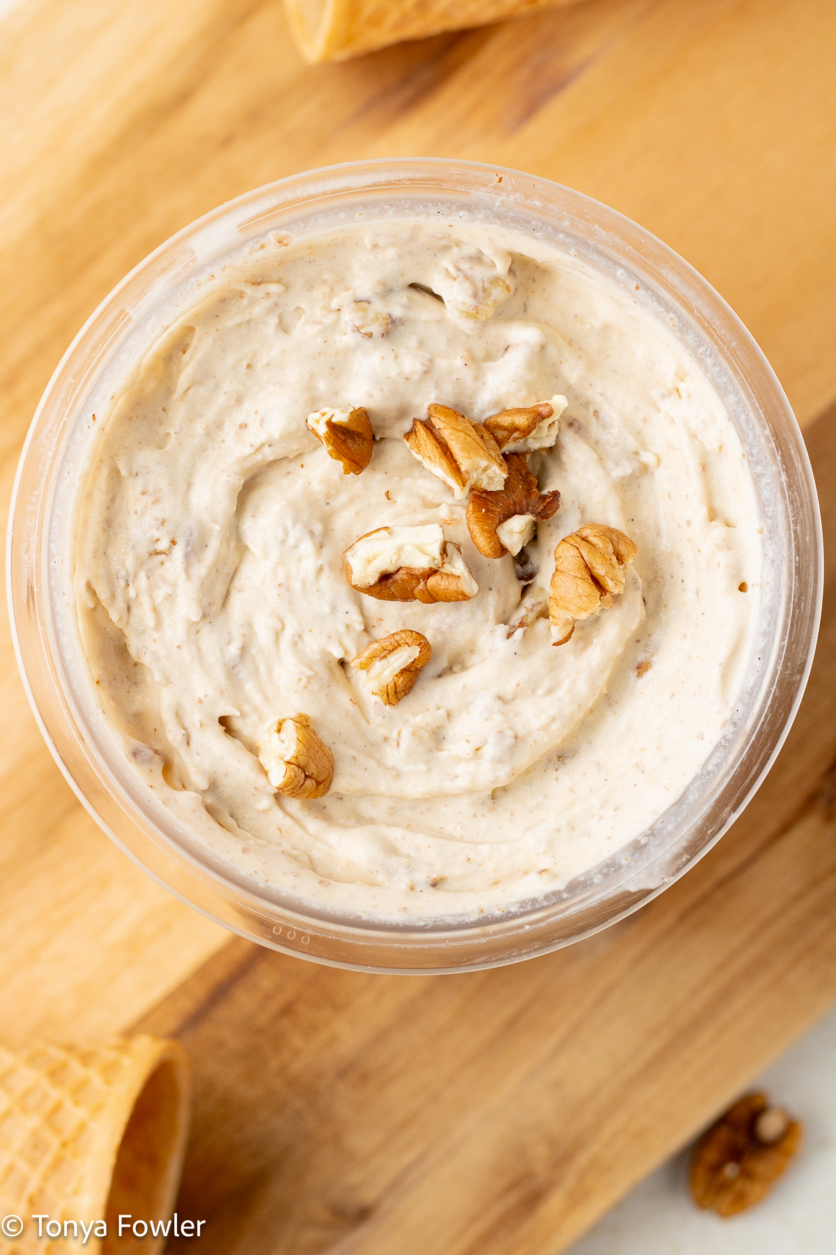 Overhead view of ice cream in a container topped with nuts.