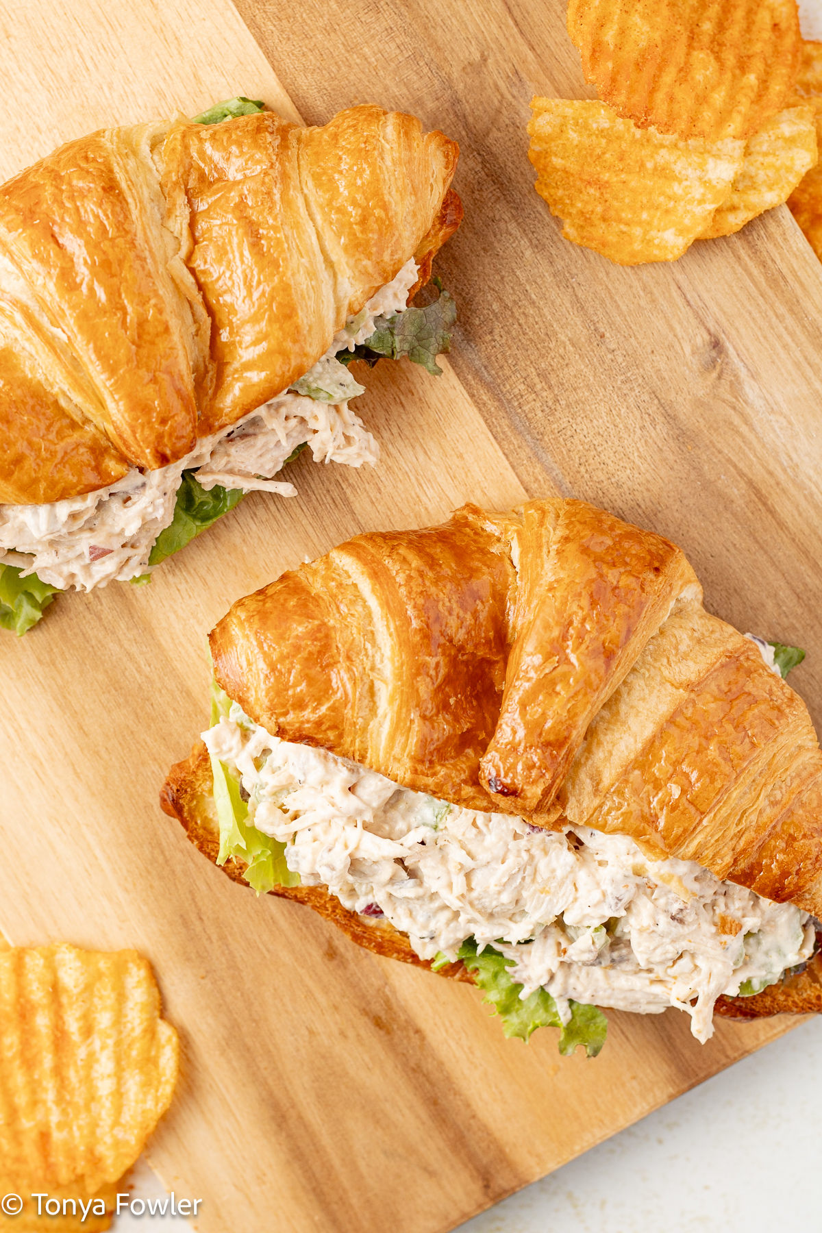 Overhead image of turkey salad sandwiches on a cutting board with potato chips.
