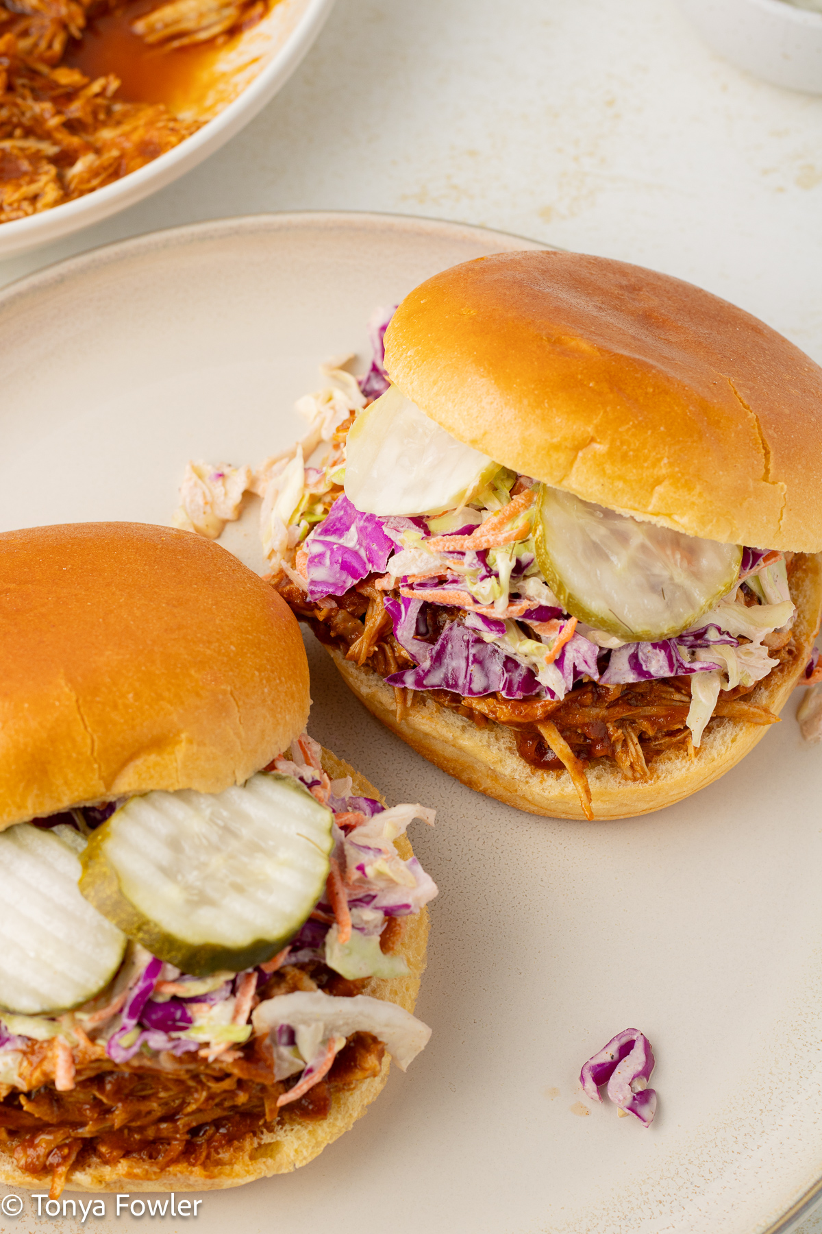 3/4 view of bbq turkey sandwiches with coleslaw and pickles on a plate.