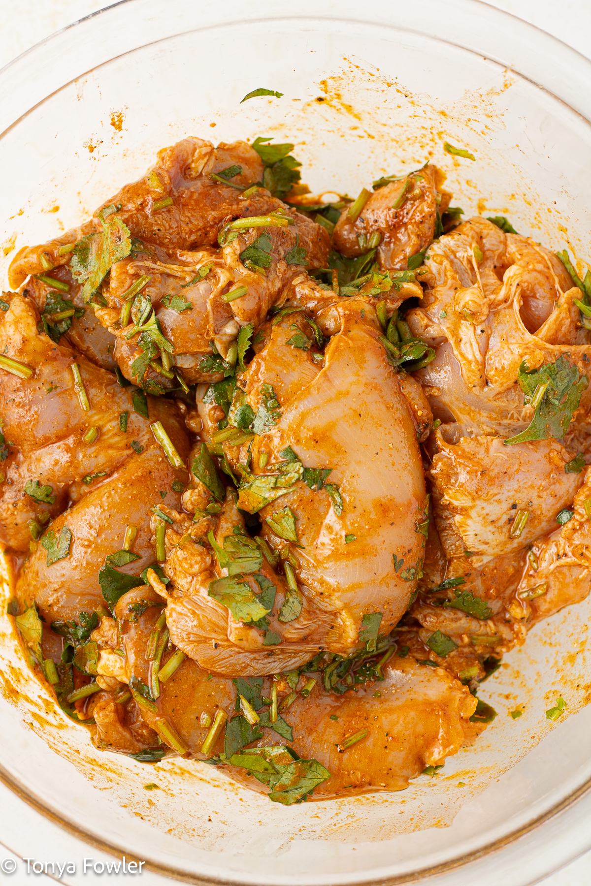 Chicken thighs in a bowl with fresh cilantro, lime juice and spices. 
