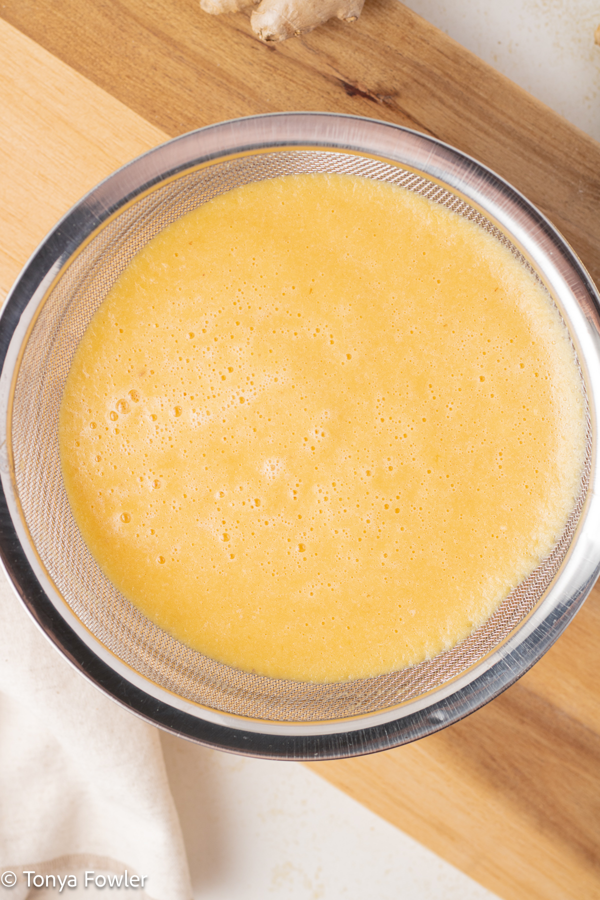Overhead view of blended fruit and ginger in a strainer.