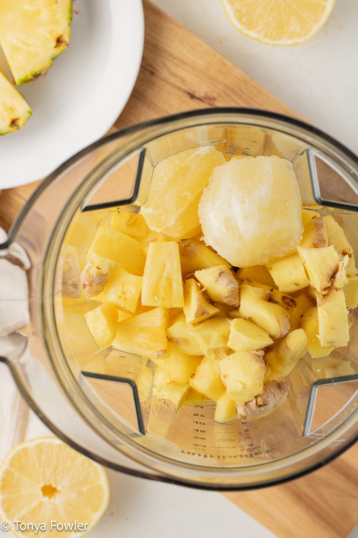 Overhead view of cut ginger, lemon and pineapple in a blender.
