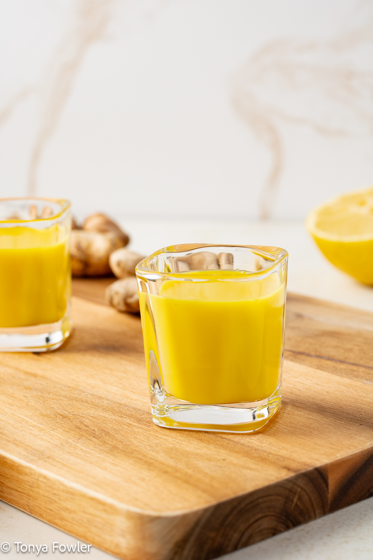 Side view of Turmeric Ginger Shots in glasses on a cutting board.