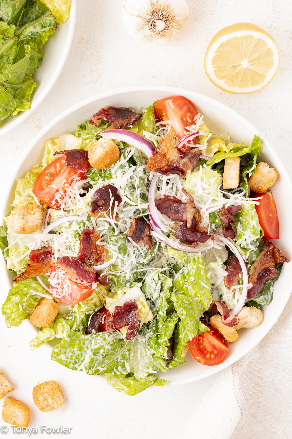 Overhead image of a Bacon Caesar Salad on a table with ingredients all around.