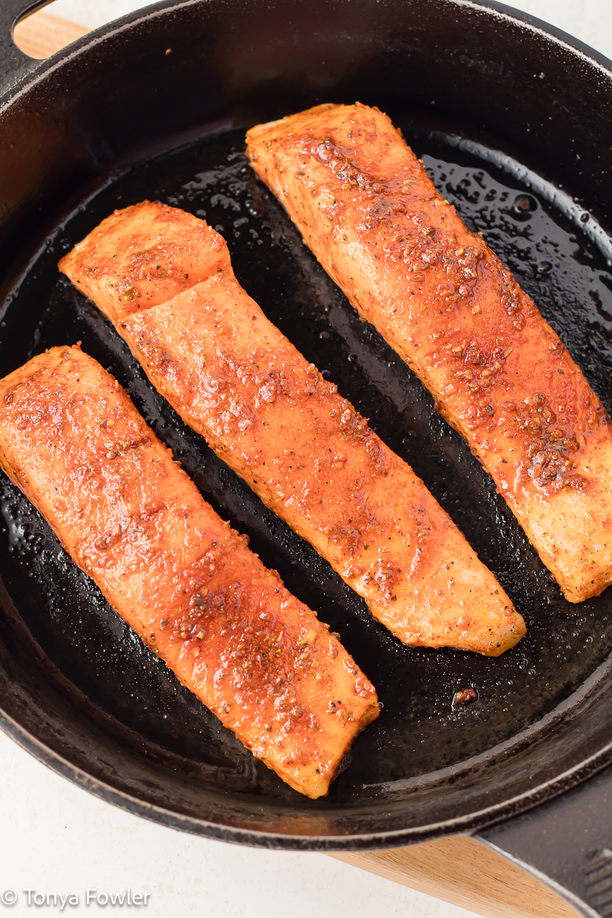 3/4 view of raw salmon fillets in a cast iron skillet. 