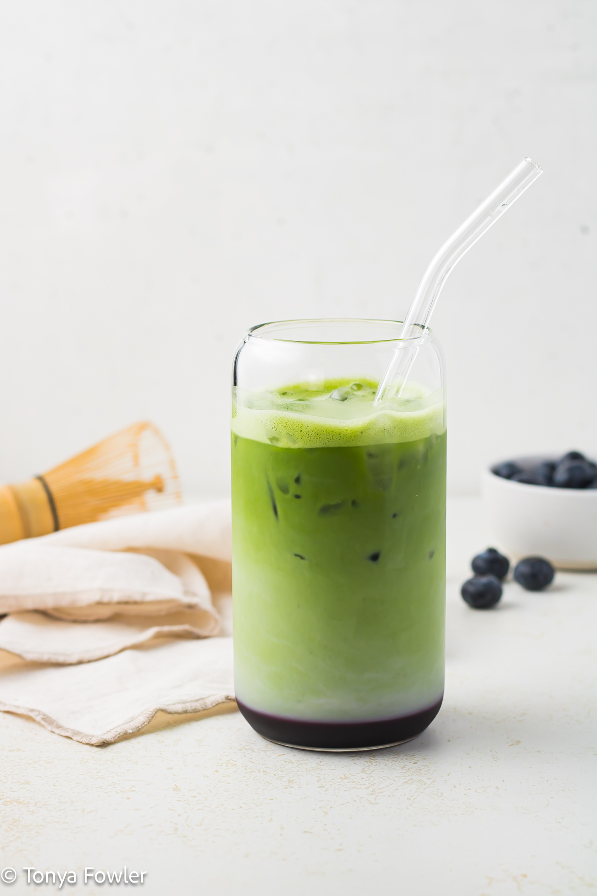 Side view of a matcha latte in a glass with blueberries on a counter.