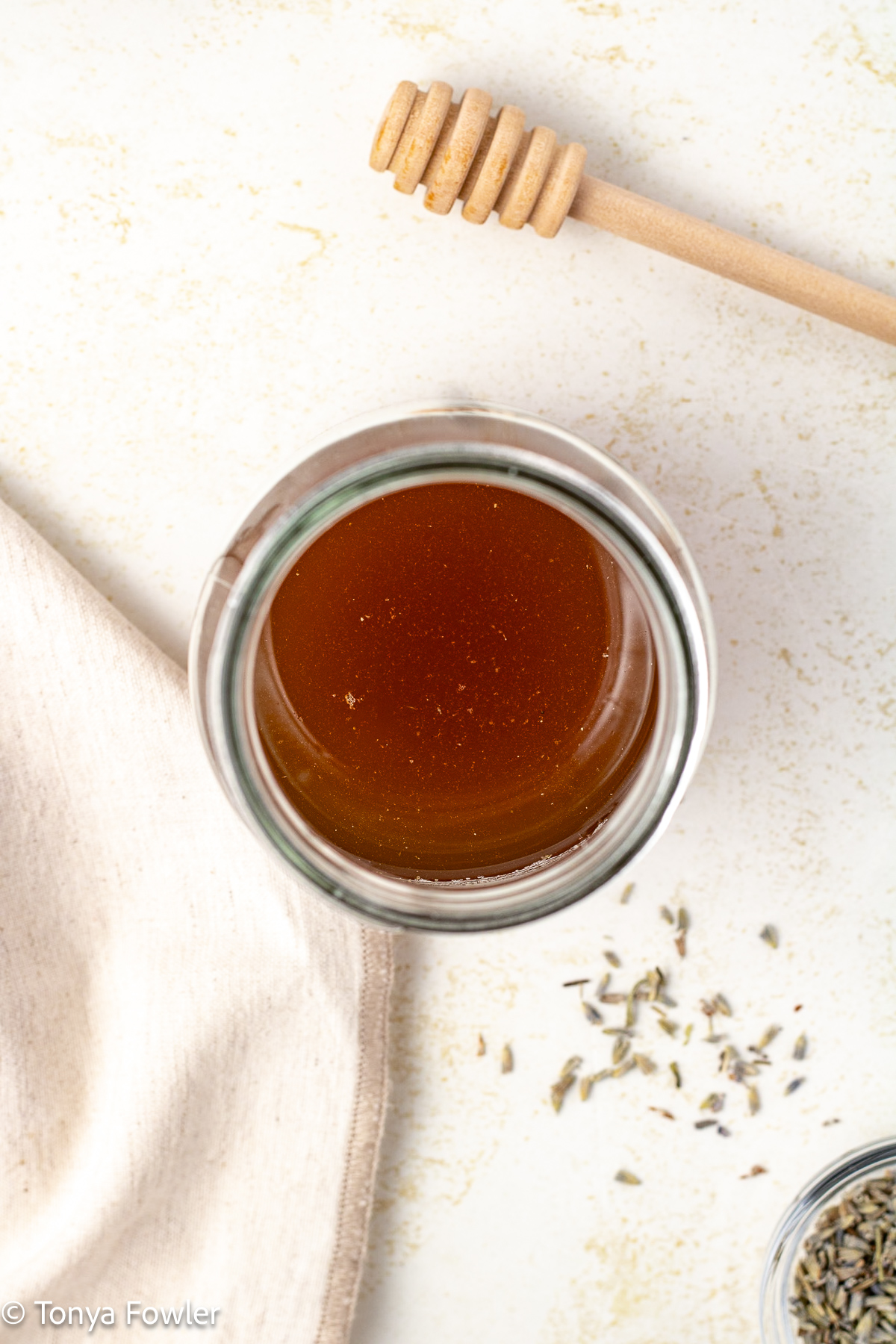 Overhead image of honey syrup in a mason jar with lavender buds and a honey dipper near by.