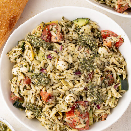 Orzo Pesto Pasta Salad in a bowl with a loaf of bread near by on a table.