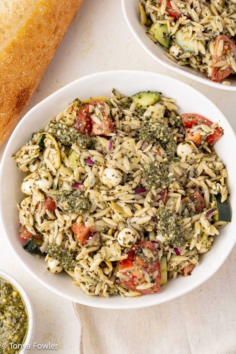 Orzo Pesto Pasta Salad in a bowl with a loaf of bread near by on a table.