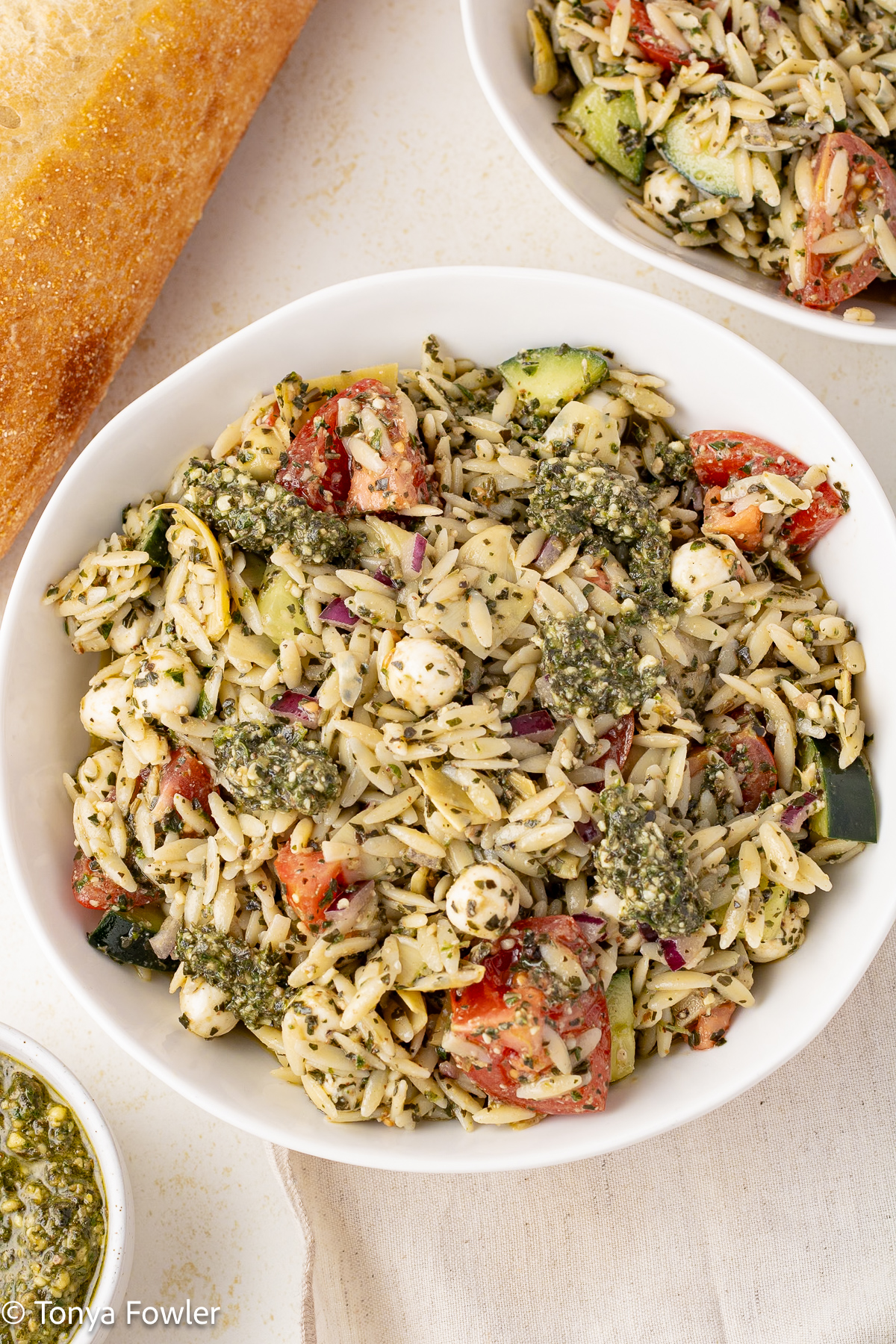 Orzo Pesto Pasta Salad in a bowl with a loaf of bread near by on a table.