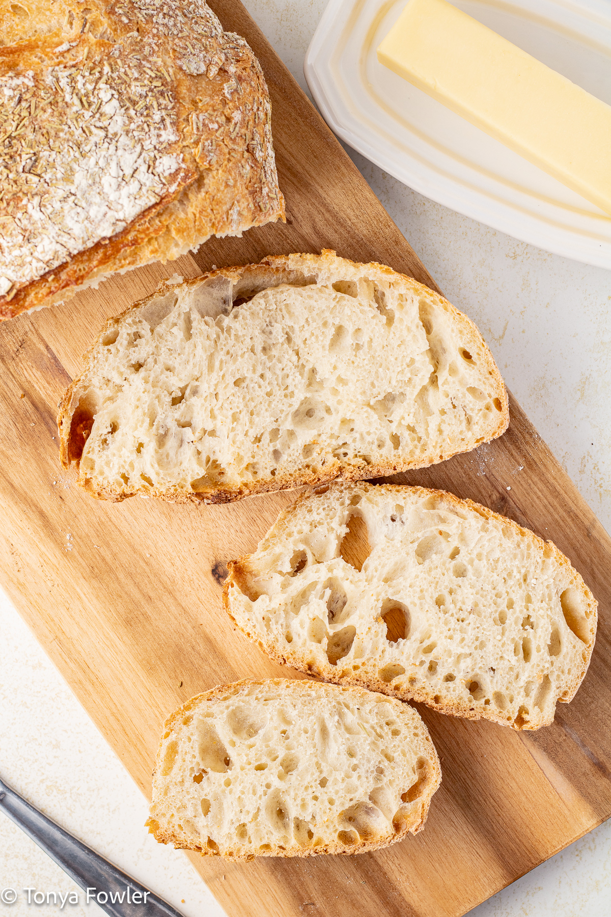 Overhead view of sliced bread on a cutting board with butter and a knife near by.