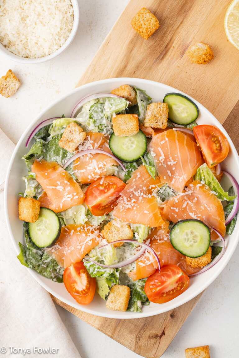 Overhead image of Smoked Salmon Caesar Salad in a bowl with croutons and grated cheese all around.