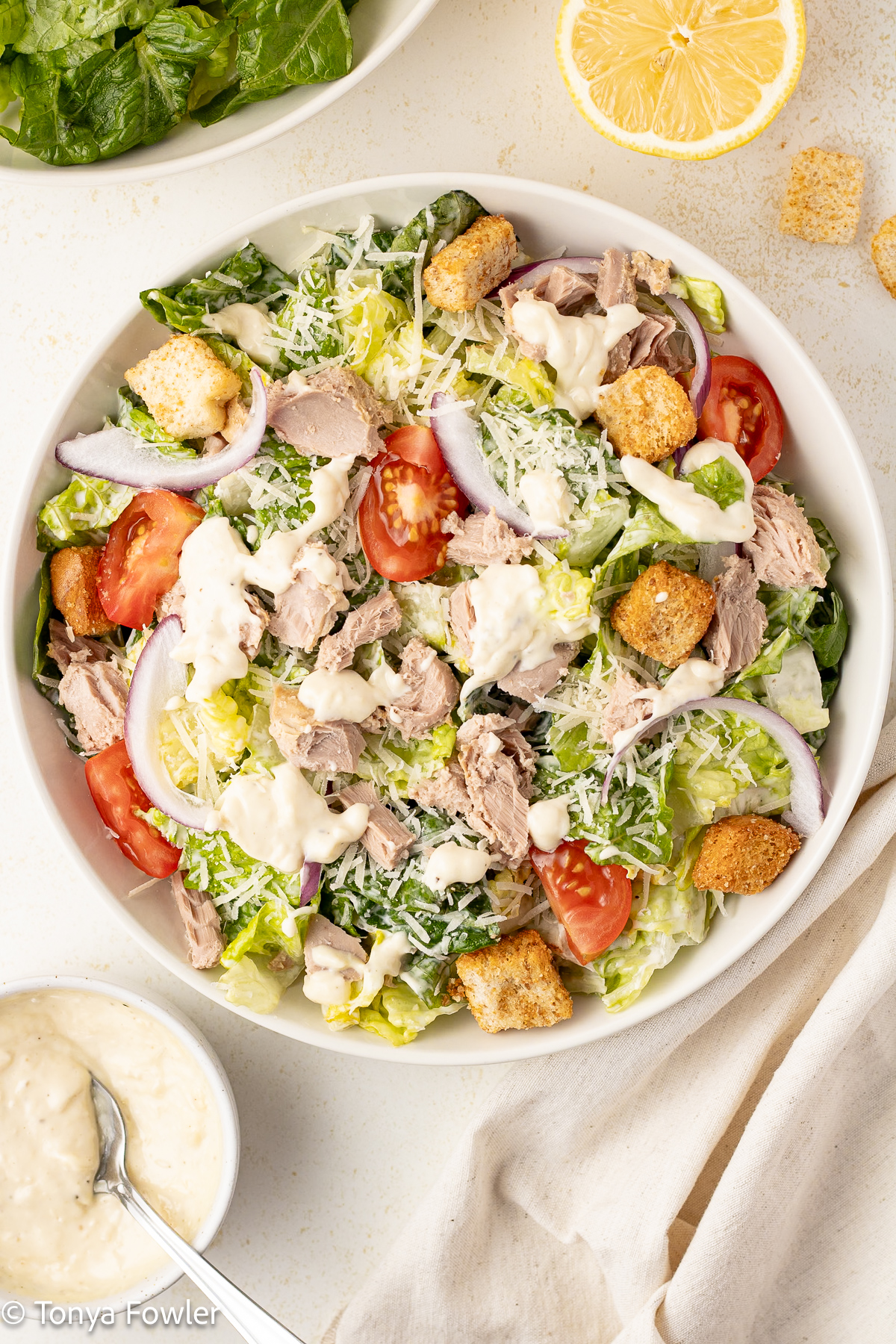 Overhead image of tuna caesar salad in a bowl with dressing and lettuce near by.
