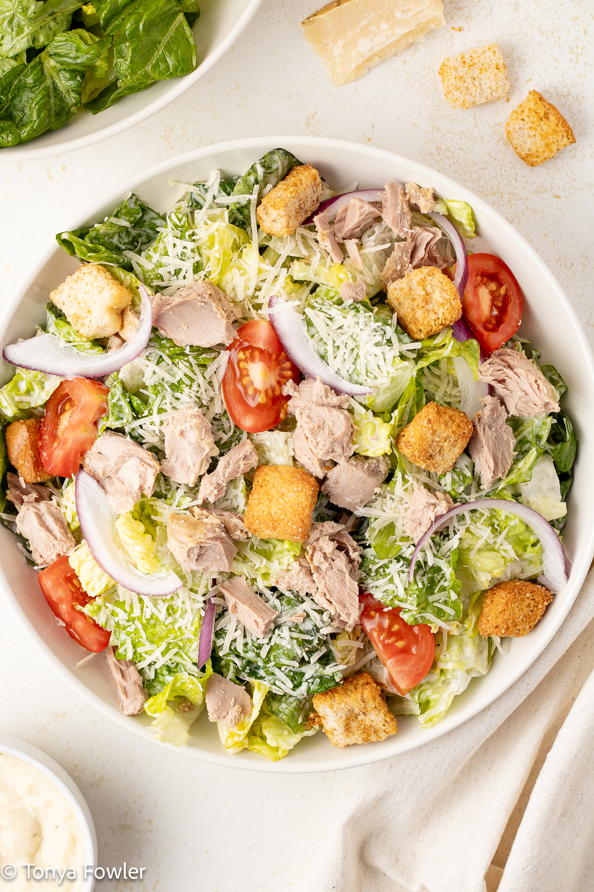 Overhead view of a salad in a bowl with ingredients all around the table. 