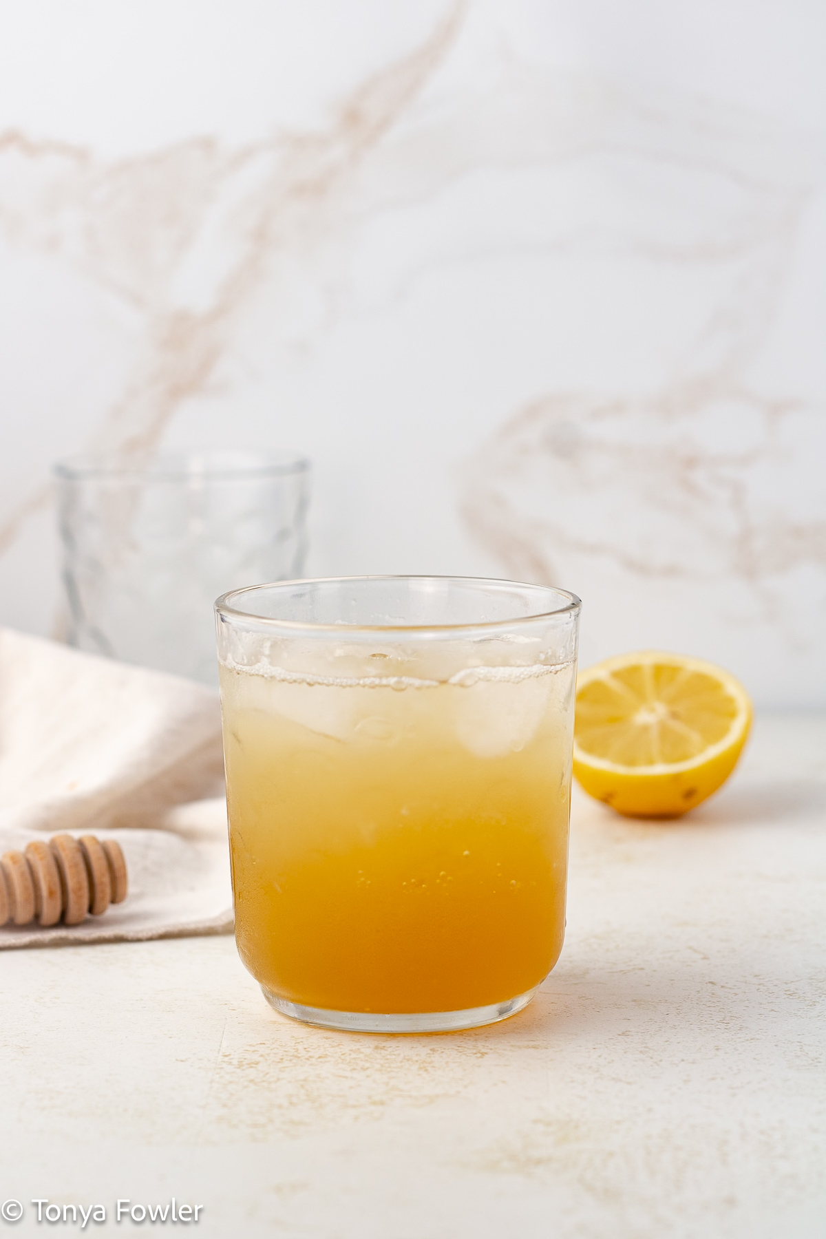 Straight on view of lemon honey mocktail in a glass with a lemon in the background.