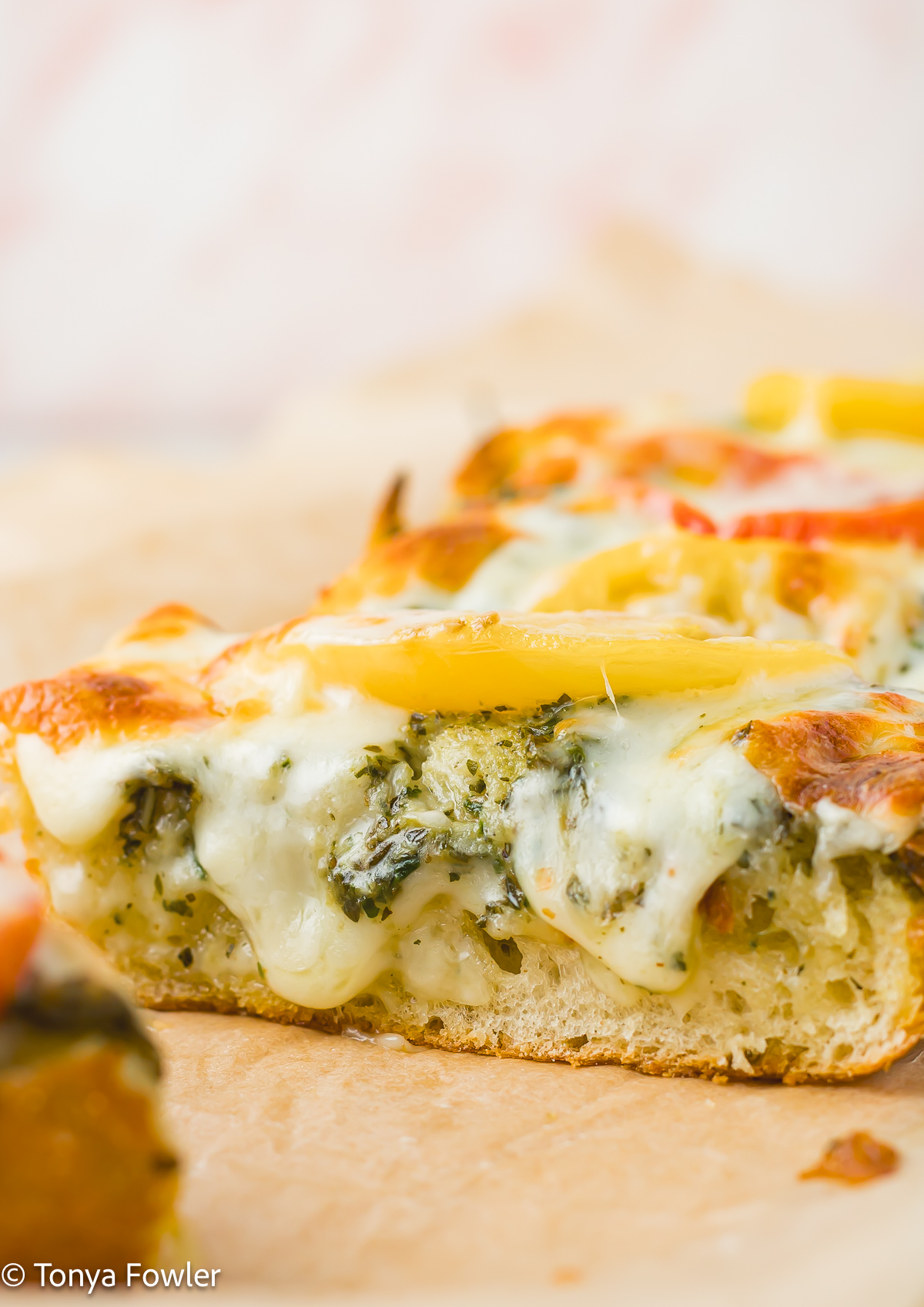 Straight on view of a slice of cheesy pesto bread.