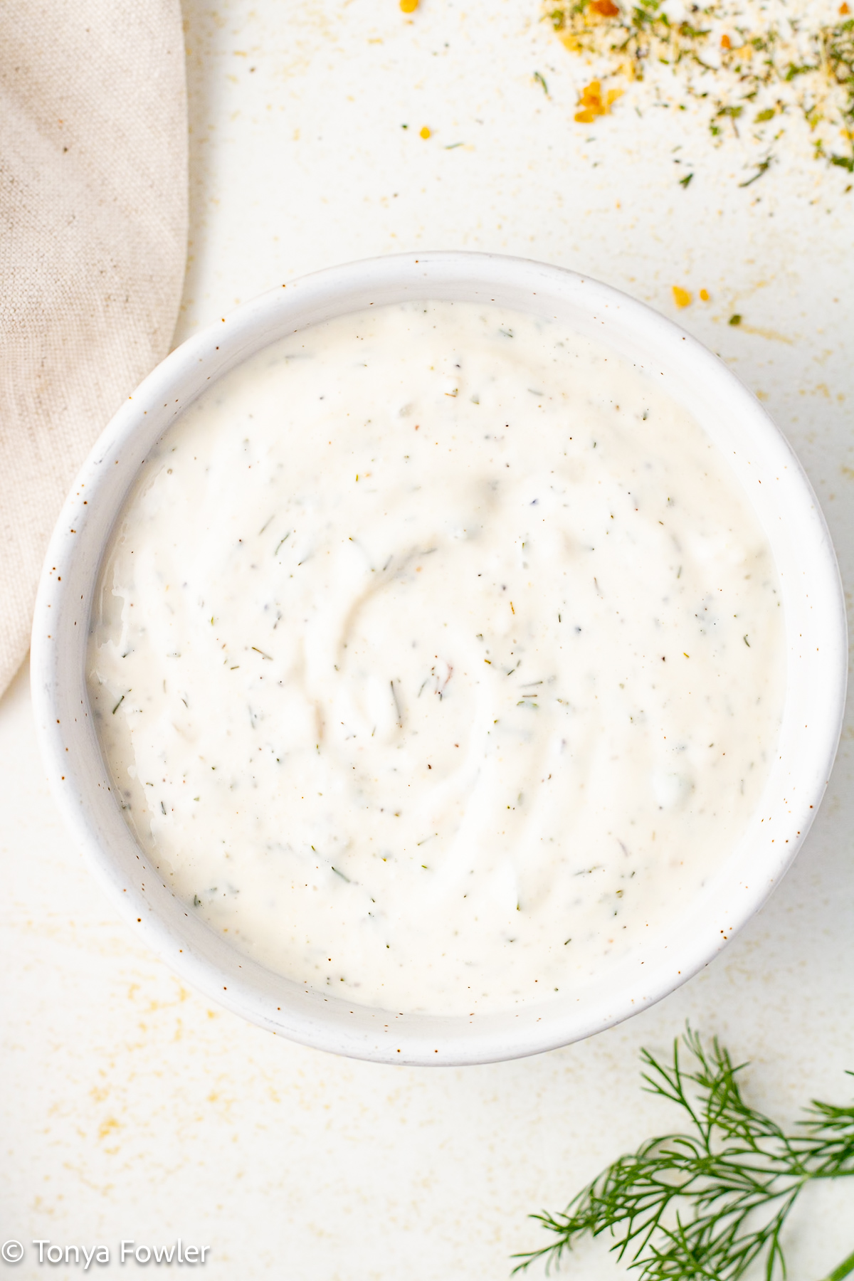 Ranch dressing in a bowl with fresh dill and seasonings all around. 